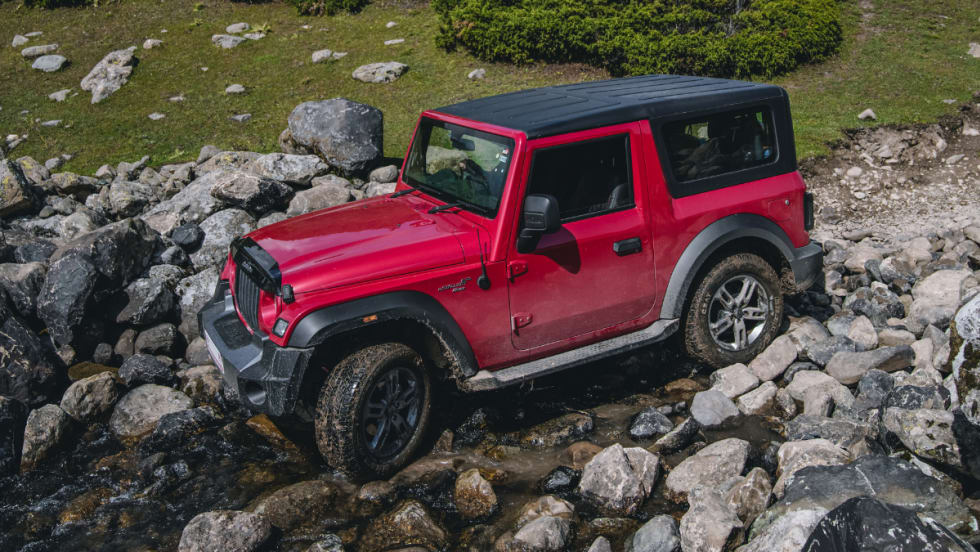 red Jeep Wrangler driving over rocky terrain