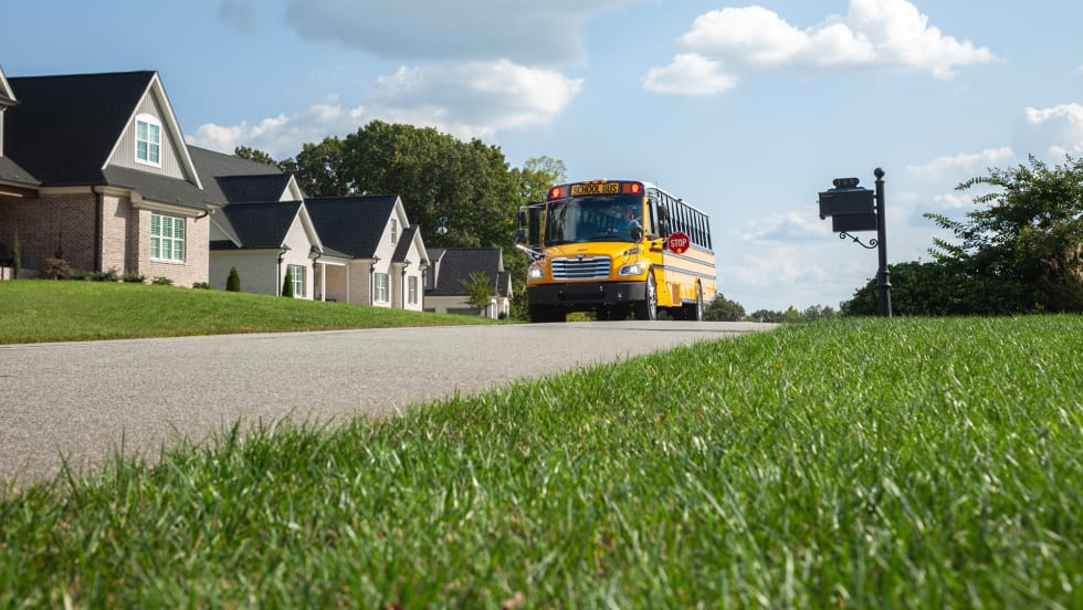 a photo of a school bus driving down a suburban street with houses in the background and green grass pictured