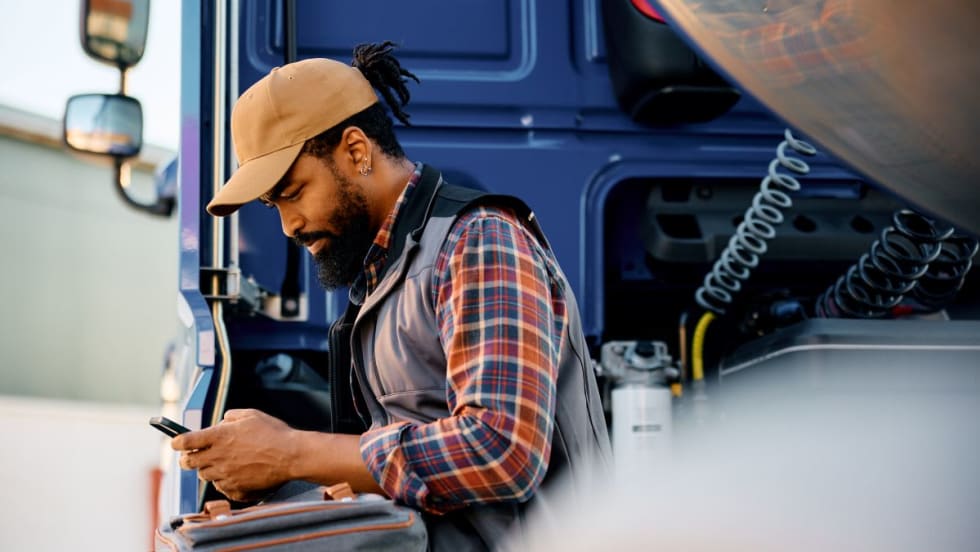 Male truck driver in flannel shirt by truck using his smartphone