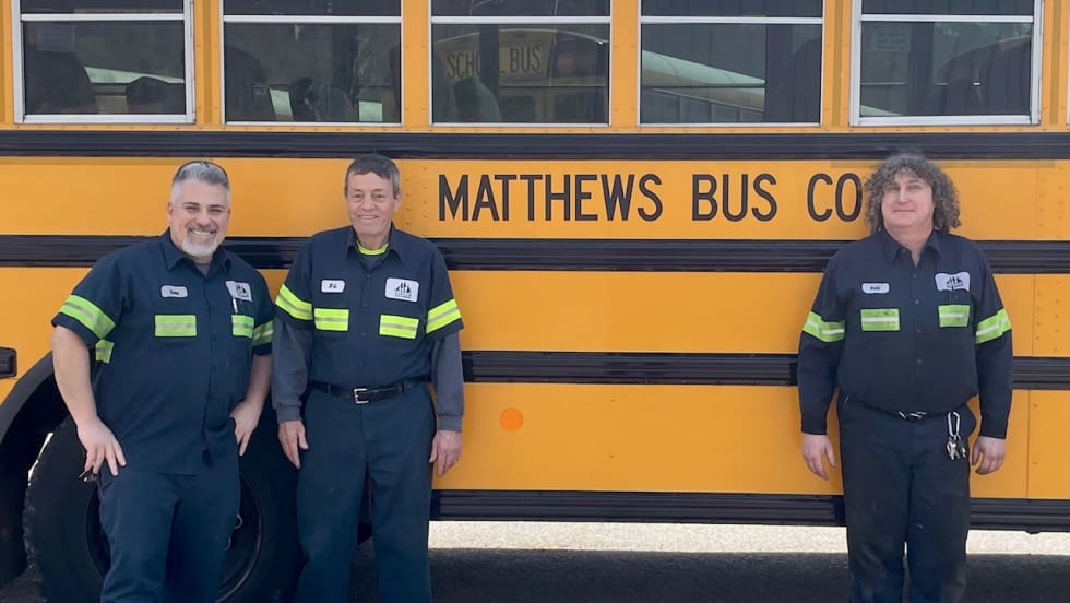 Matthews Bus Company maintenance team members stand in front of a yellow school bus, recognized by Pennsylvania State Police for fleet safety, cleanliness, and inspection performance.