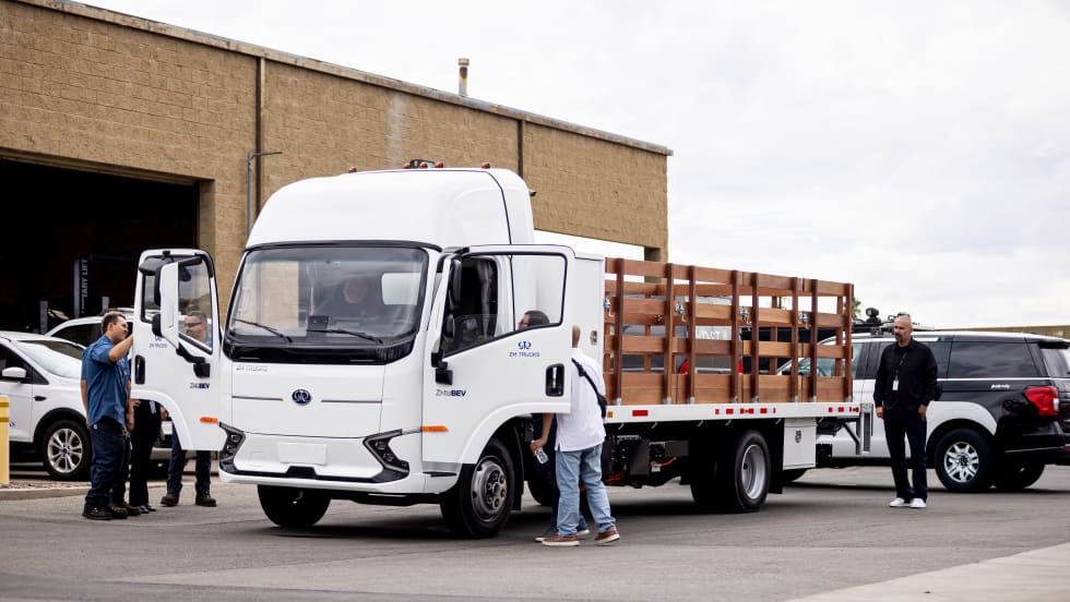 A lot of several vehicles, with the central vehicle being a medium-duty work truck with several workers inspecting it.