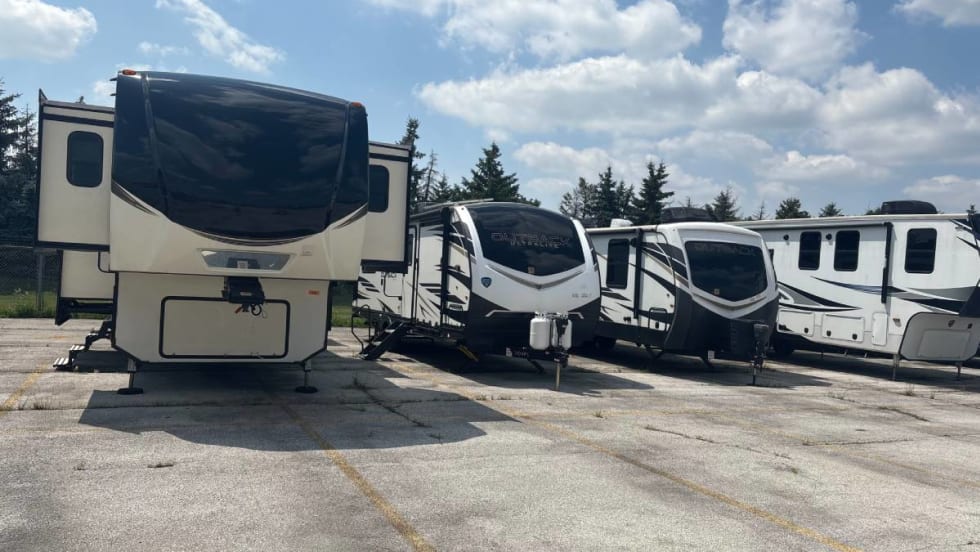 Camper trailers lined up in a parking lot underneath a blue sky with white puffy clouds. 