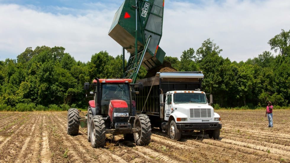 Tractor loading a farm truck in a field.