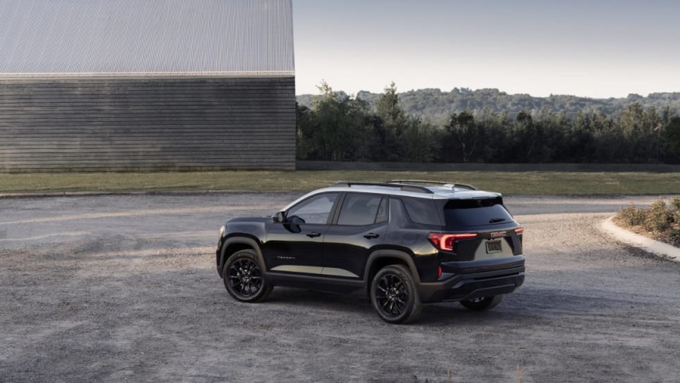 The back left side of a black 2025 GMC Terrain Elevation in front of a metal warehouse.