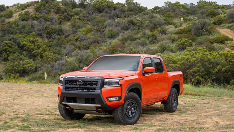 An orange Nissan Frontier in front of a hillside.