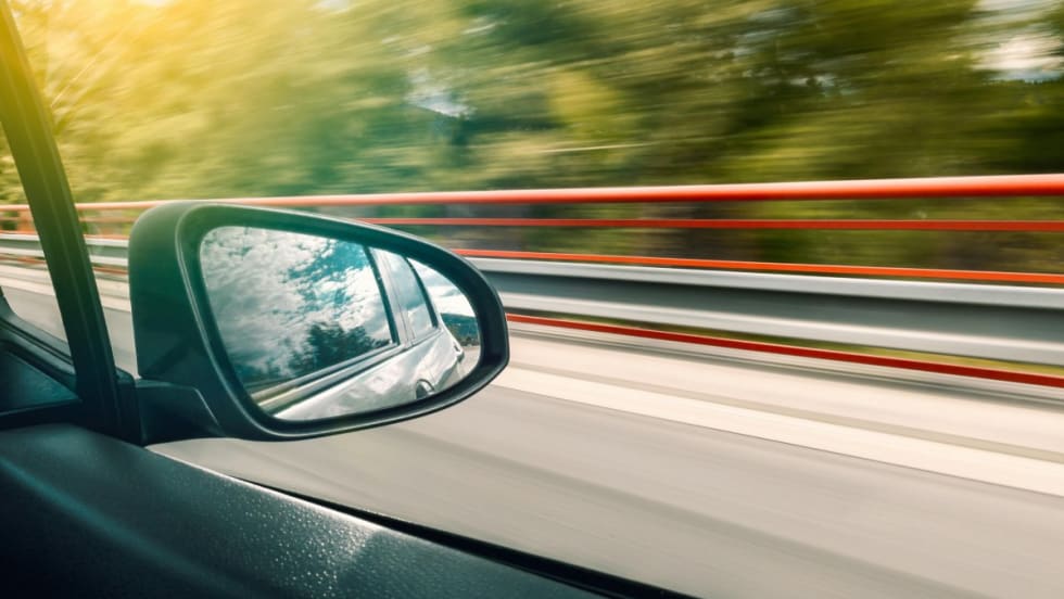 Image of a bridge and trees rushing by from inside of a moving car.