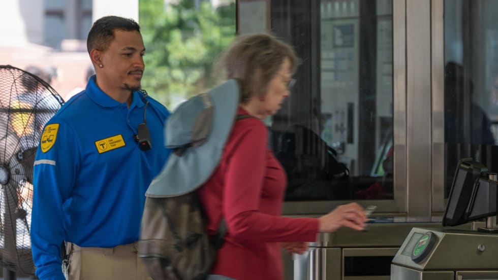 An MBTA fare engagement representative looks on while a woman pays for her subway fare.
