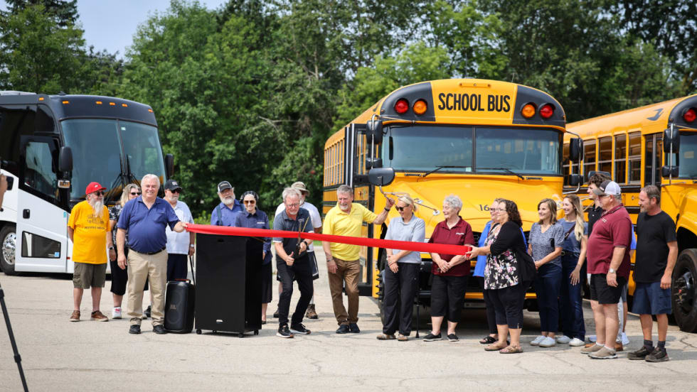 A crowd stands behind a red ribbon being cut.