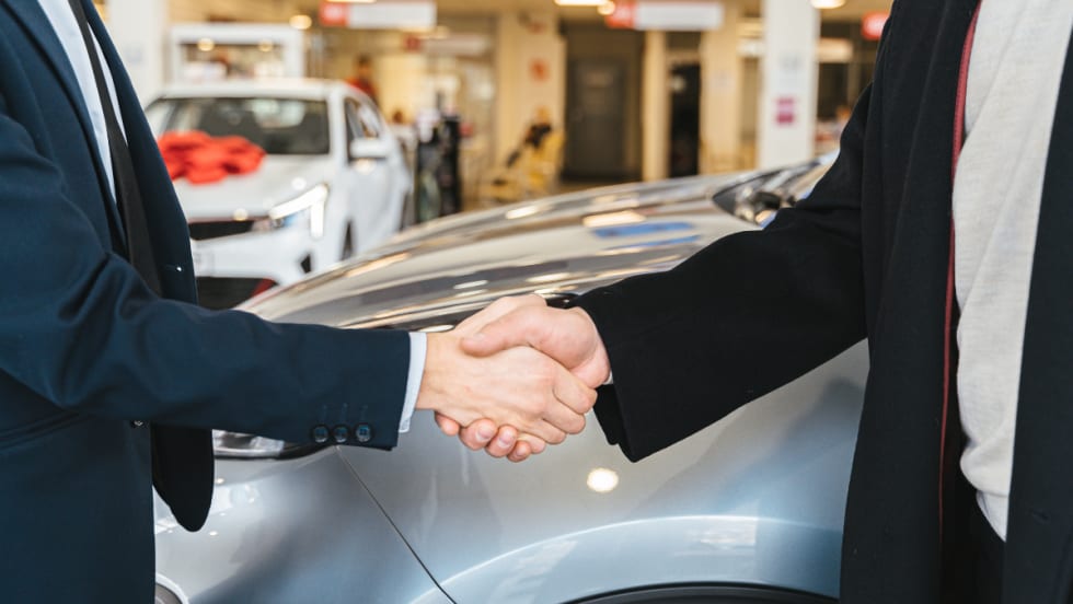 two men shaking hands in front of cars