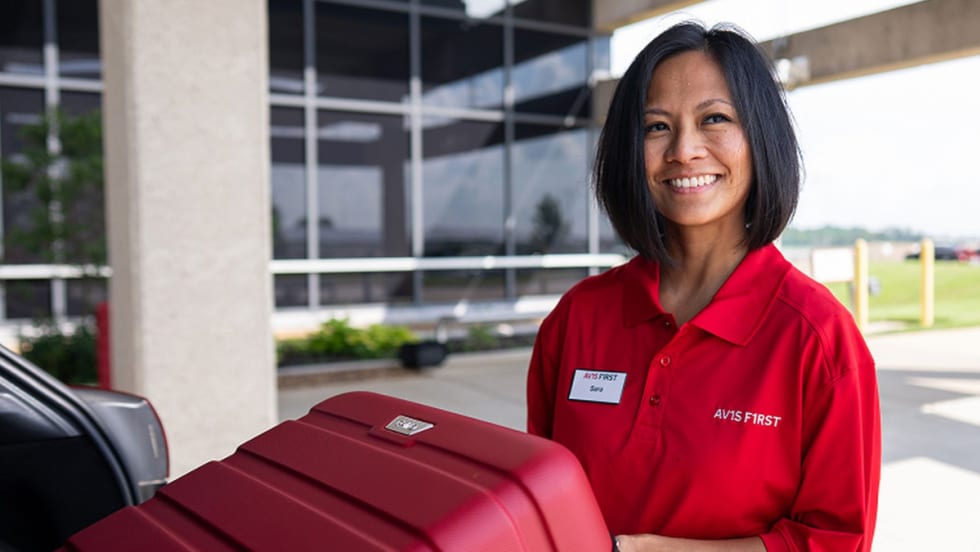 An Avis rep unloads luggage from a rental car as part of first-class service.