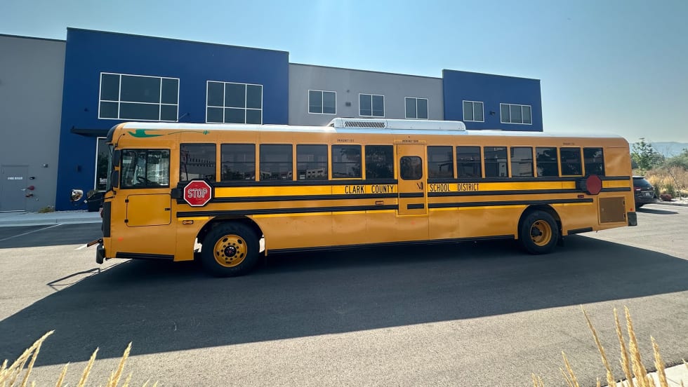 A yellow Blue Bird electric school bus sits in front of a school building.