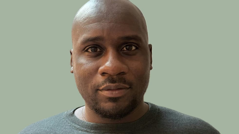 Bald man in gray sweater against sage green background