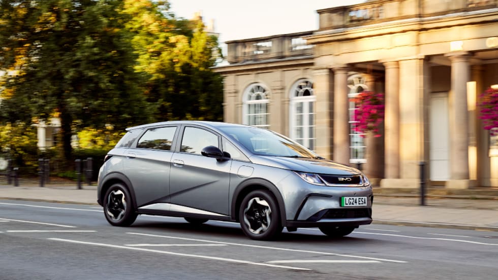 Photo of a gray BYD Dolphin sub-compact electric vehicle in front of a columned historic building.