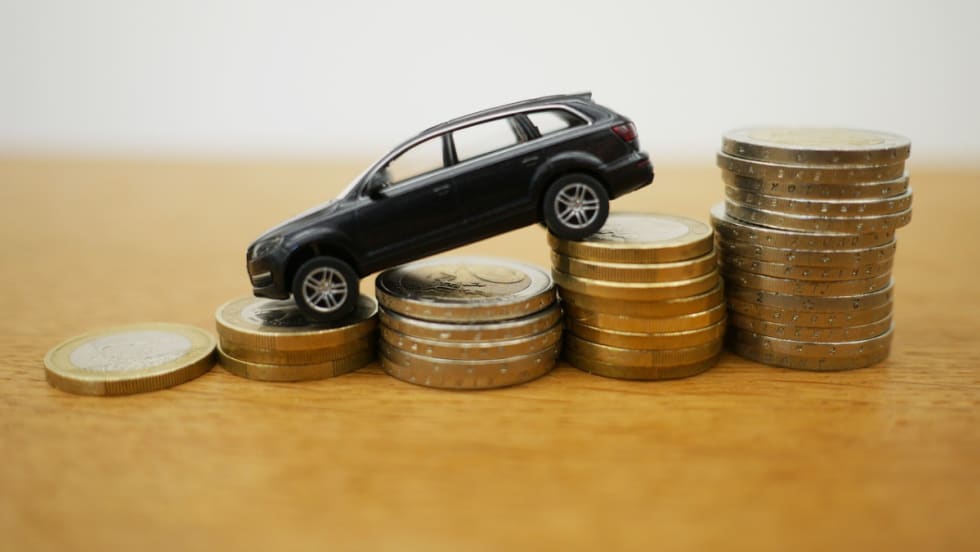 A black CUV tilted downward on stacks of descending gold coins.