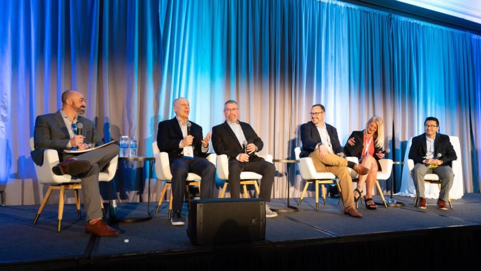 Six panelists on a stage in front of a blue curtain.