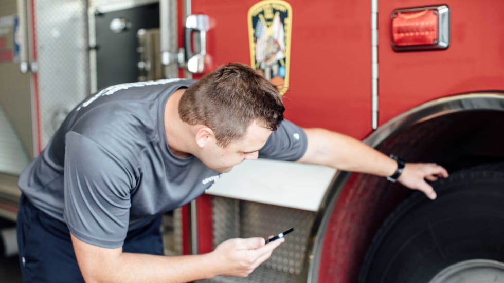 A firefighter with a phone looking at a fire truck wheel.