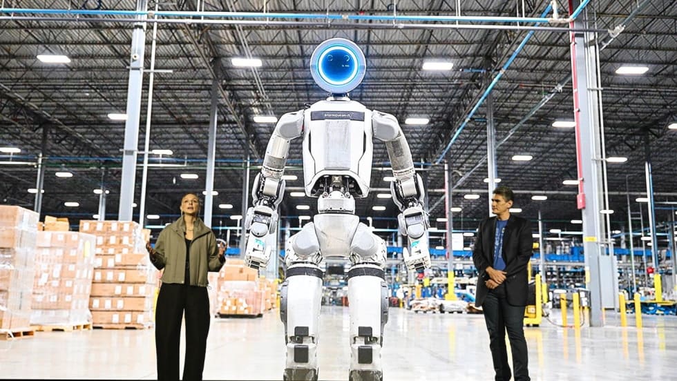 Boston Dynamics executives in front of image of Atlas humanoid robot in a warehouse setting