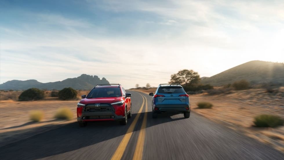 Both new Toyota Corolla Cross models driving on a road. 