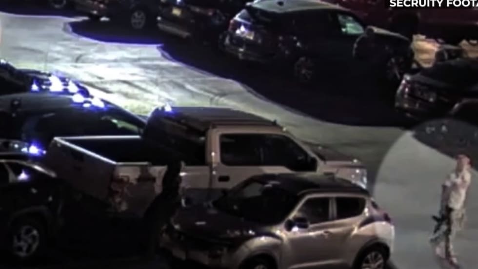 Night security footage of parking lot with multiple vehicles and blue emergency lights