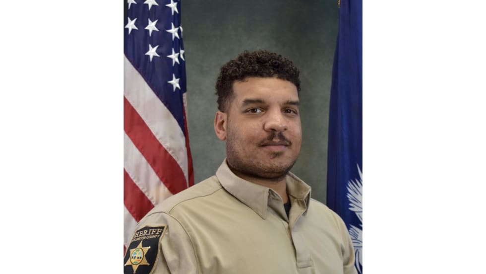 Sheriff's deputy in tan uniform posing with American and state flags