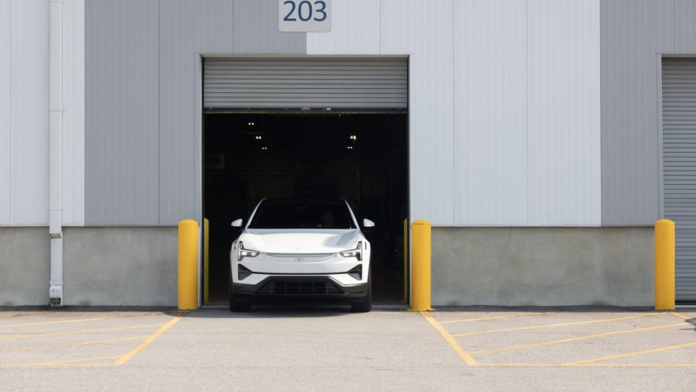 An image of the front end of a white Polestar 3 parking within the open frame of a commercial garage door. 