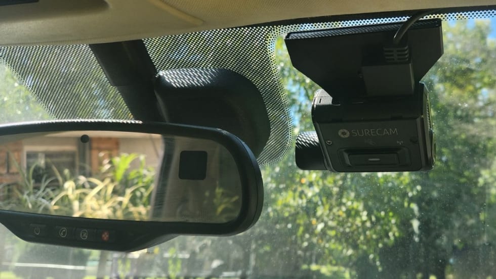 An image of the rearview mirror and a SureCam dashcam attached to the inside of a car windshield.