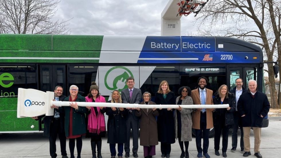 A group of people pose in front of a battery electric transit bus.