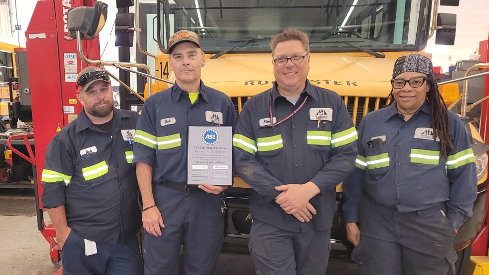 Durham School Services Ann Arbor team with ASE Blue Seal of Excellence plaque in front of a school bus
