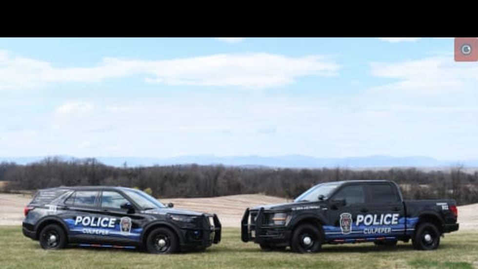 Two Culpeper Police vehicles, an SUV and pickup, display a new Blue Ridge Mountain-inspired design while parked on grass with a scenic landscape in the background.