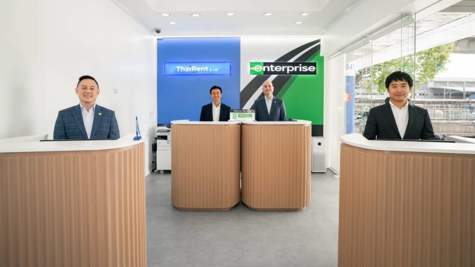 Representatives of Thai Rent-A-Car stand at airport service counters. 