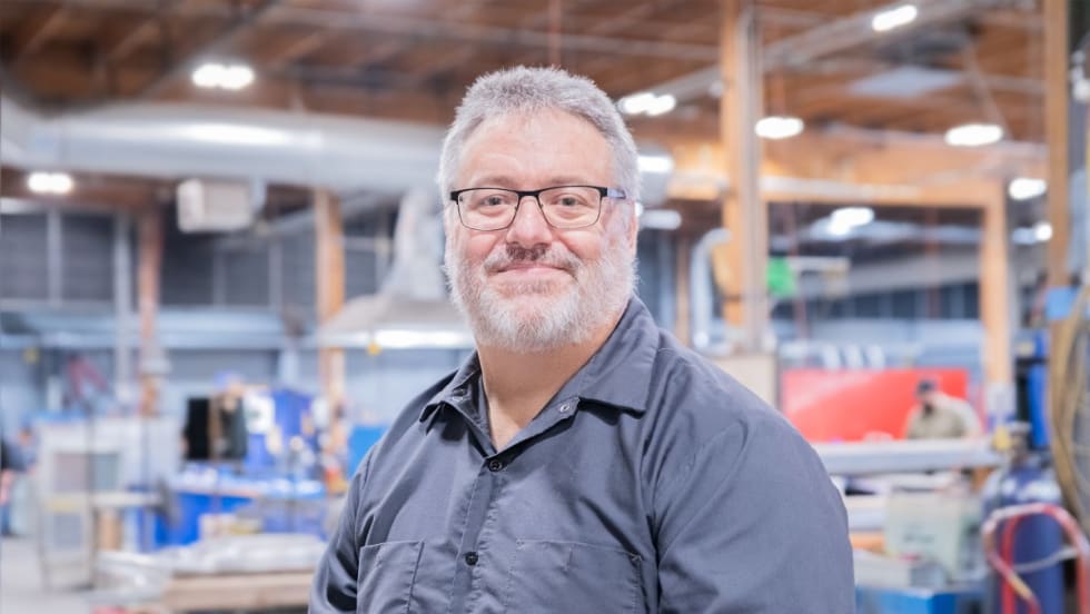 A professional portrait of Bruce Birdsell in a workshop/warehouse.