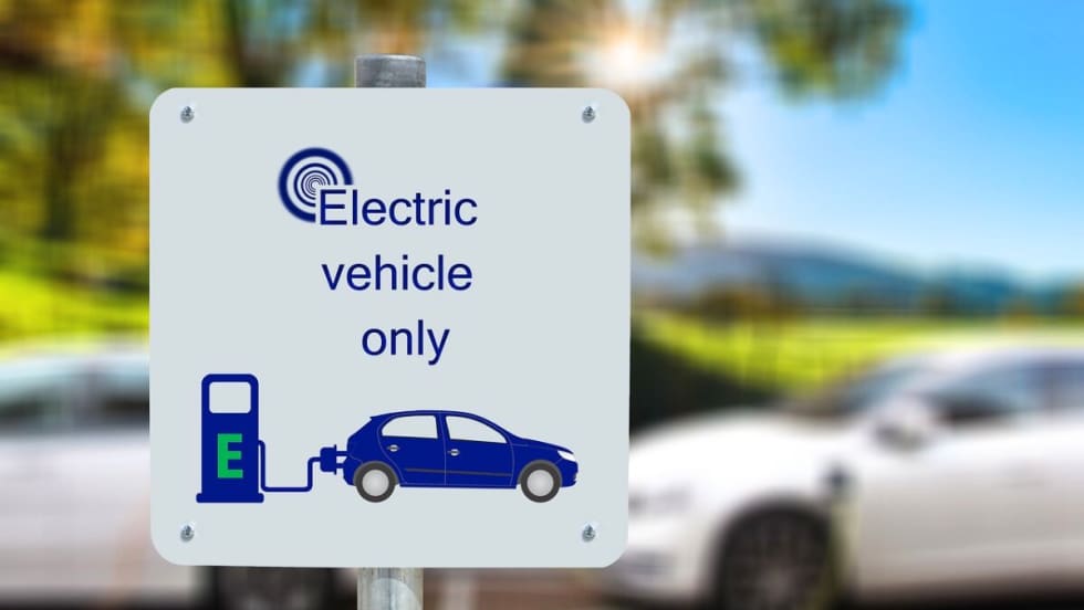 Image of a sign that says "Electric Vehicle Only" in front of charging vehicles.