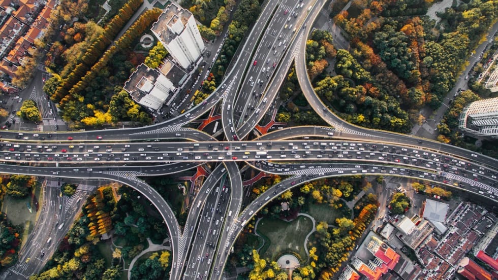 Aerial view of interconnected highways and exit ramps surrounded by trees, streets, and buildings.