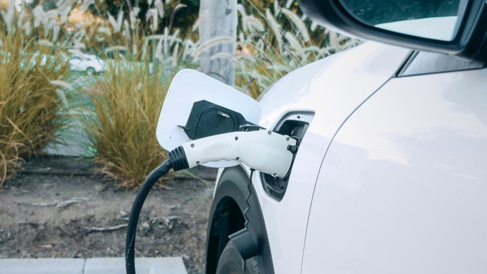 A white passenger car being fueled via electric charging.