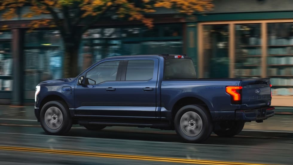 Blue Ford F-150 Lightning driving down the road in front of shops