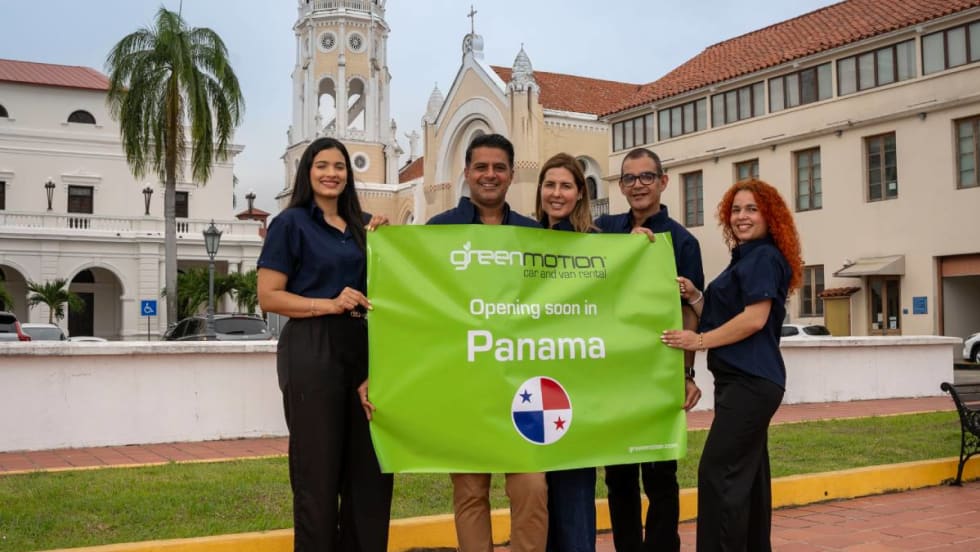 Five Panama-based Green Motion employees holding a green banner sign in front of historical building in Panama City, Panama.