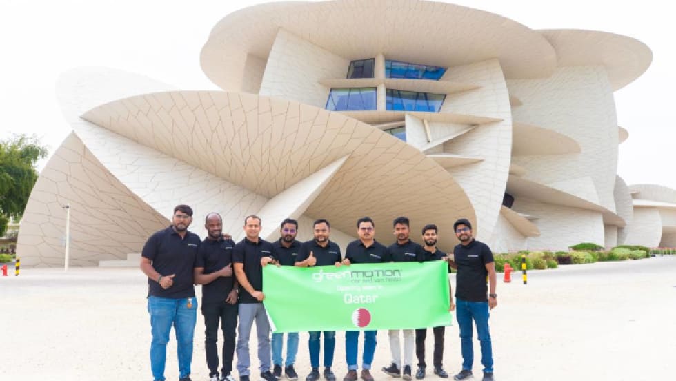 Green Motion team in front of Doah landmark with green banner.