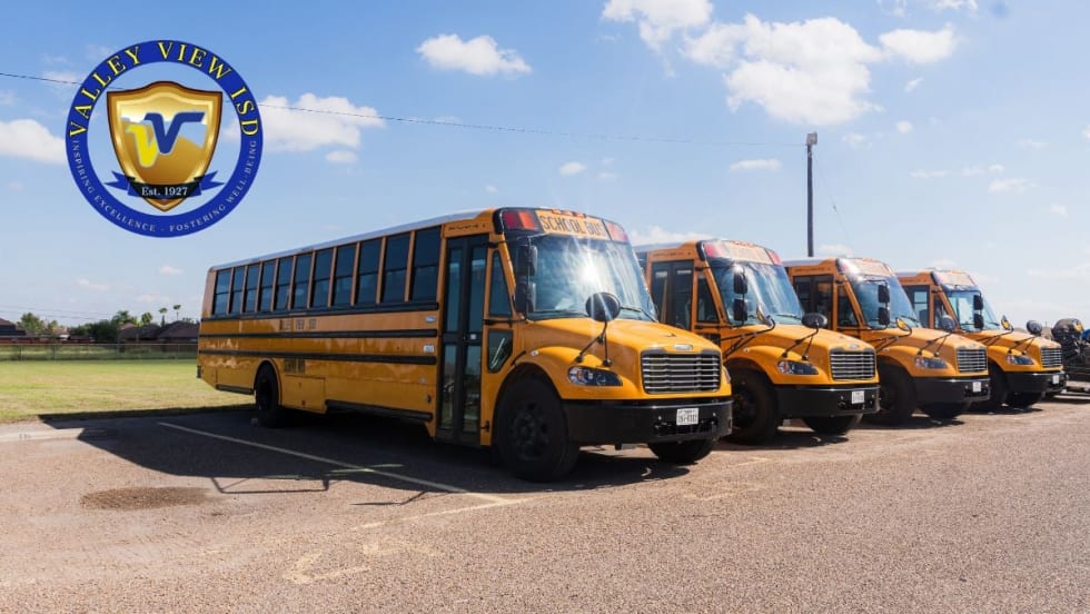 A row of yellow Valley View ISD electric school buses parked outdoors with the district logo in the corner of the image.