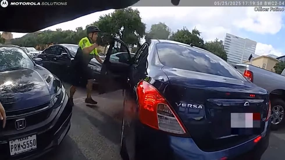 Dashcam view of traffic stop with police officer near dark blue Nissan Versa