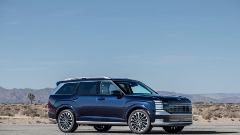 A dark blue full-size SUV parked on a desert road, with sleek modern styling, large alloy wheels, and a chrome-accented grille, set against a backdrop of dry desert landscape.