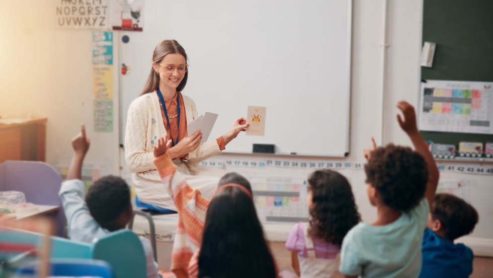 A female teacher sitting in front of elementary school classroom, giving a lesson to several students.
