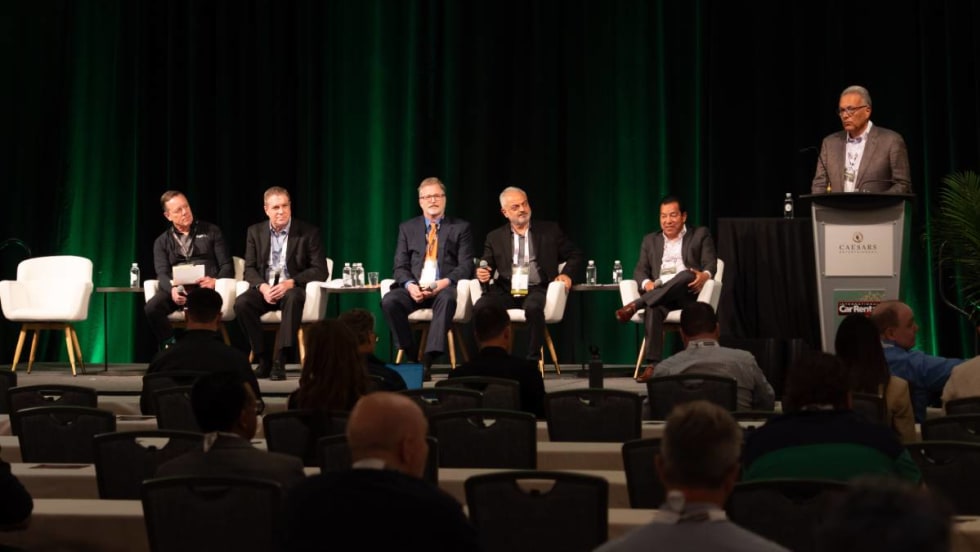 Five panelists sitting in white chairs and a moderator at the podium on stage at ICRS