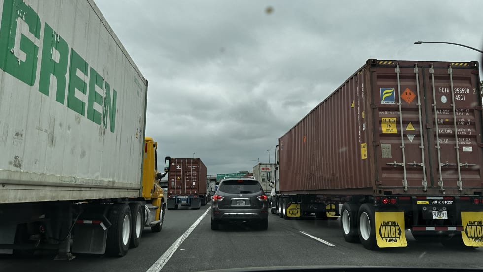 A passenger car stuck in traffic on highway next to big rigs.