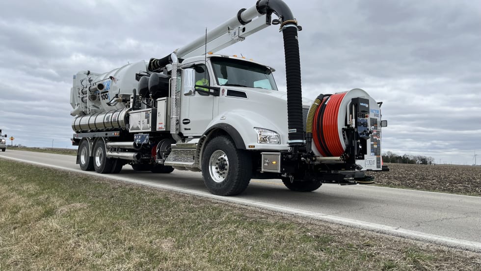 A white Vactor 2100i is seen on the side of the road, with the new longer hose positioned up front.
