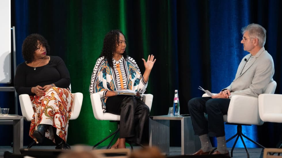 Two women and a man sit and talk on a stage.