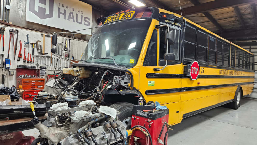 A school bus in a maintenance bay with the engine exposed.