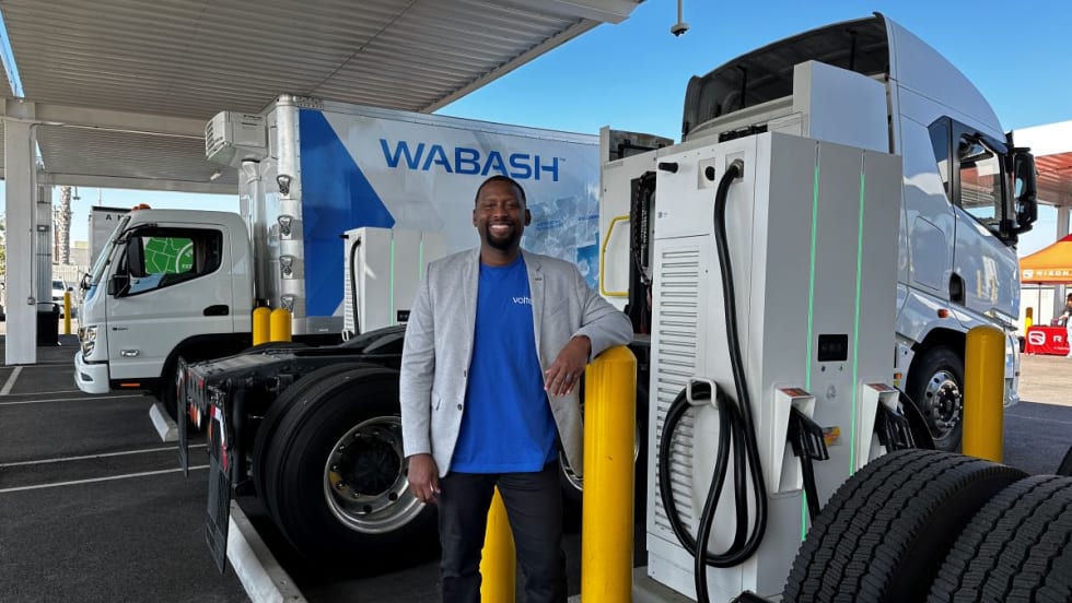 Man stands in electric truck charging depot.