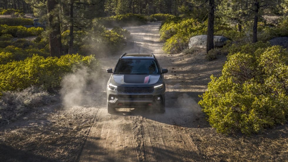 A 2025 Jeep Compass Trailhawk driving on a dirt road in a forest.