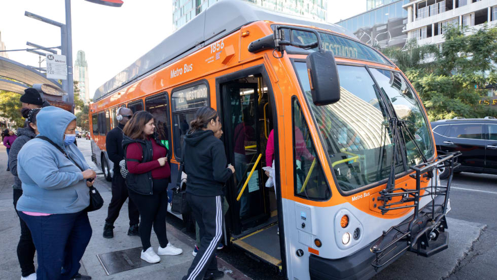 Riders board an orange and gray LA Metro bus.