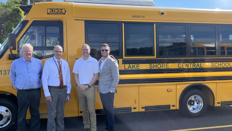 District official posing with a RIDE electric school bus. 